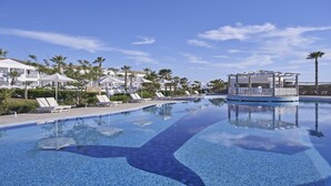 Una piscina con sillones de descanso, una cabaña y vistas a los edificios del complejo.