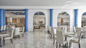 A spacious dining area with white chairs and tables, blue columns, and a marble floor.