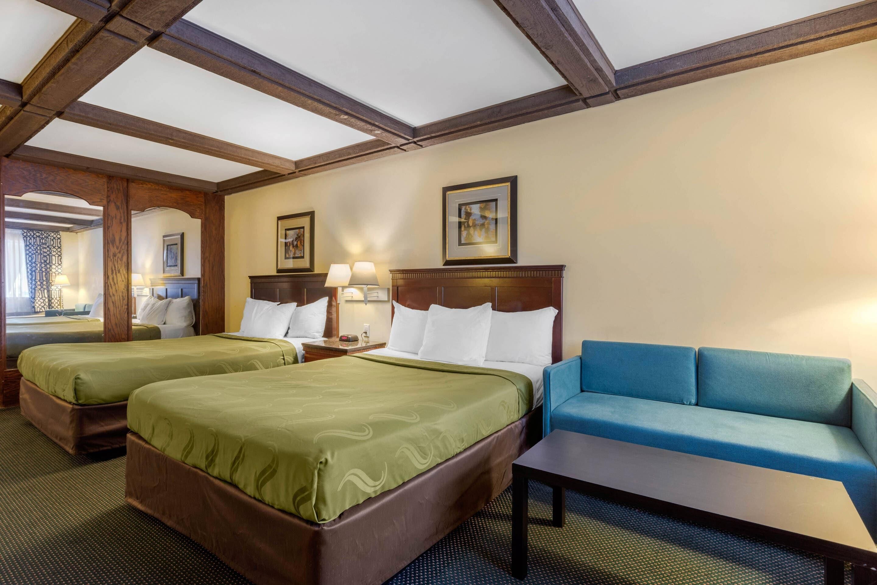 A hotel room with two beds, a sofa, a small table, and a nightstand with lamps.