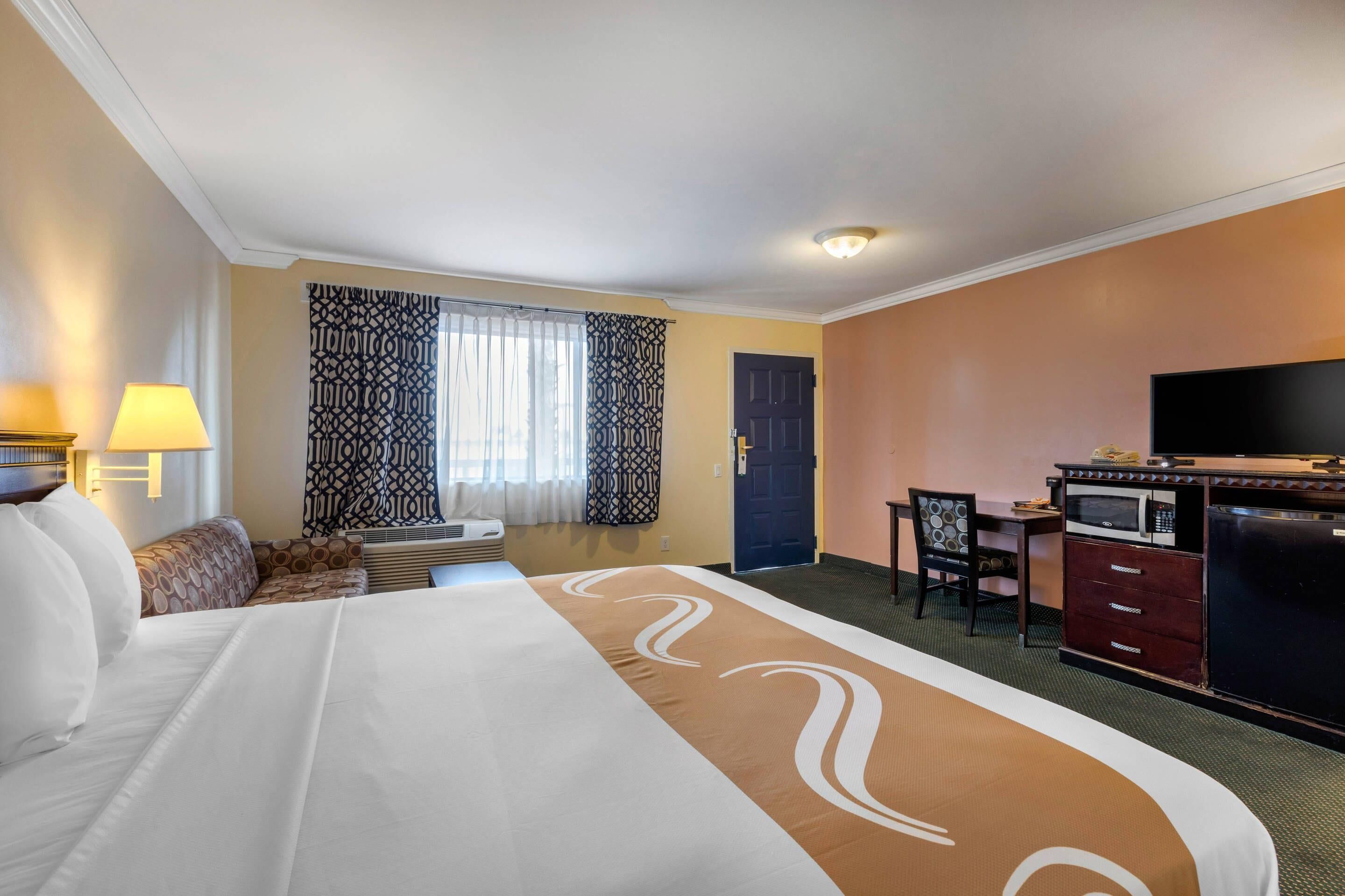 A hotel room with a large bed, a desk, a television, and a microwave.