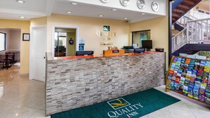 Un espace d’accueil avec un comptoir en pierre, des horloges et une enseigne indiquant « Quality Inn ».
