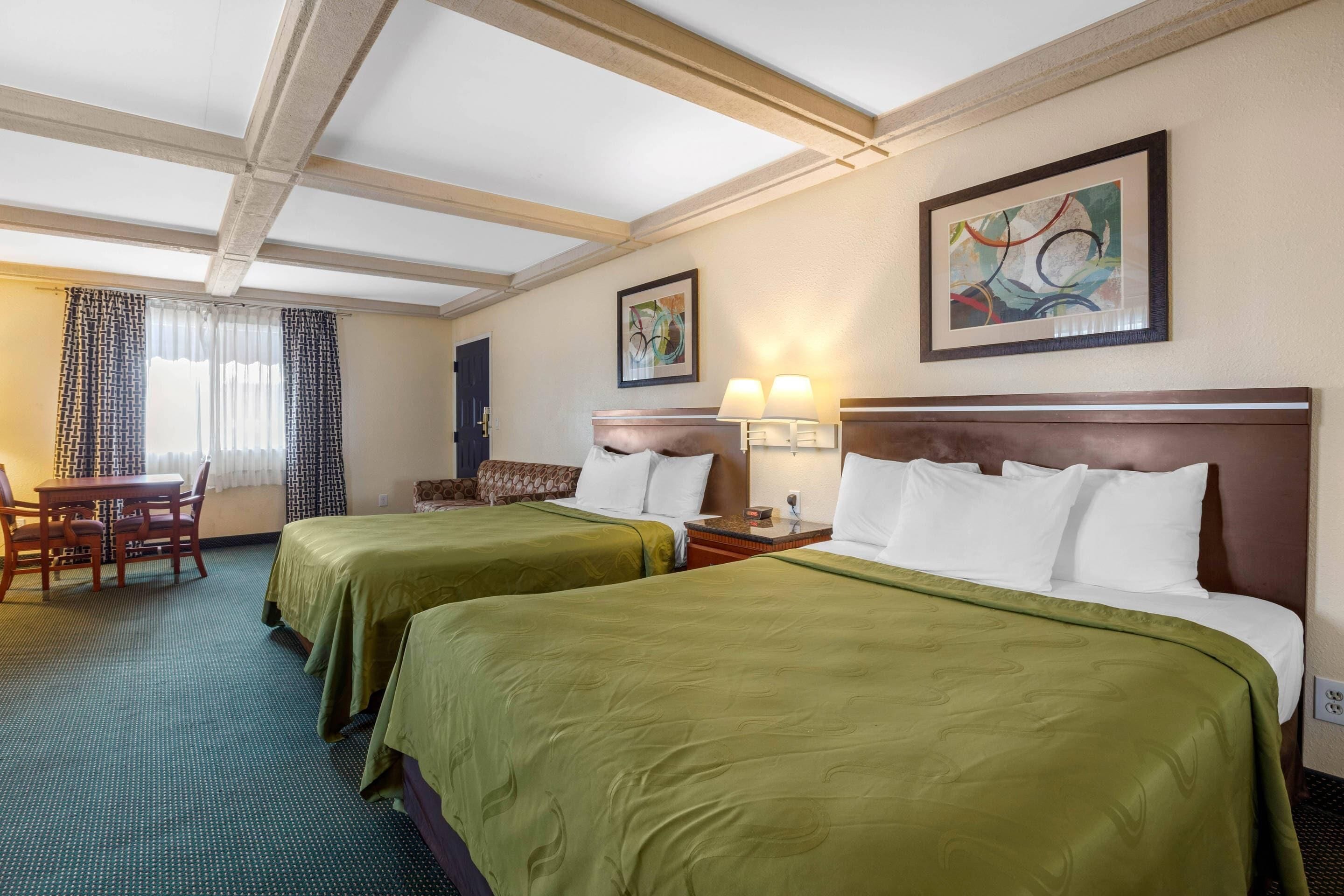 A hotel room with two beds, a desk, and a chair. There are two paintings on the walls.