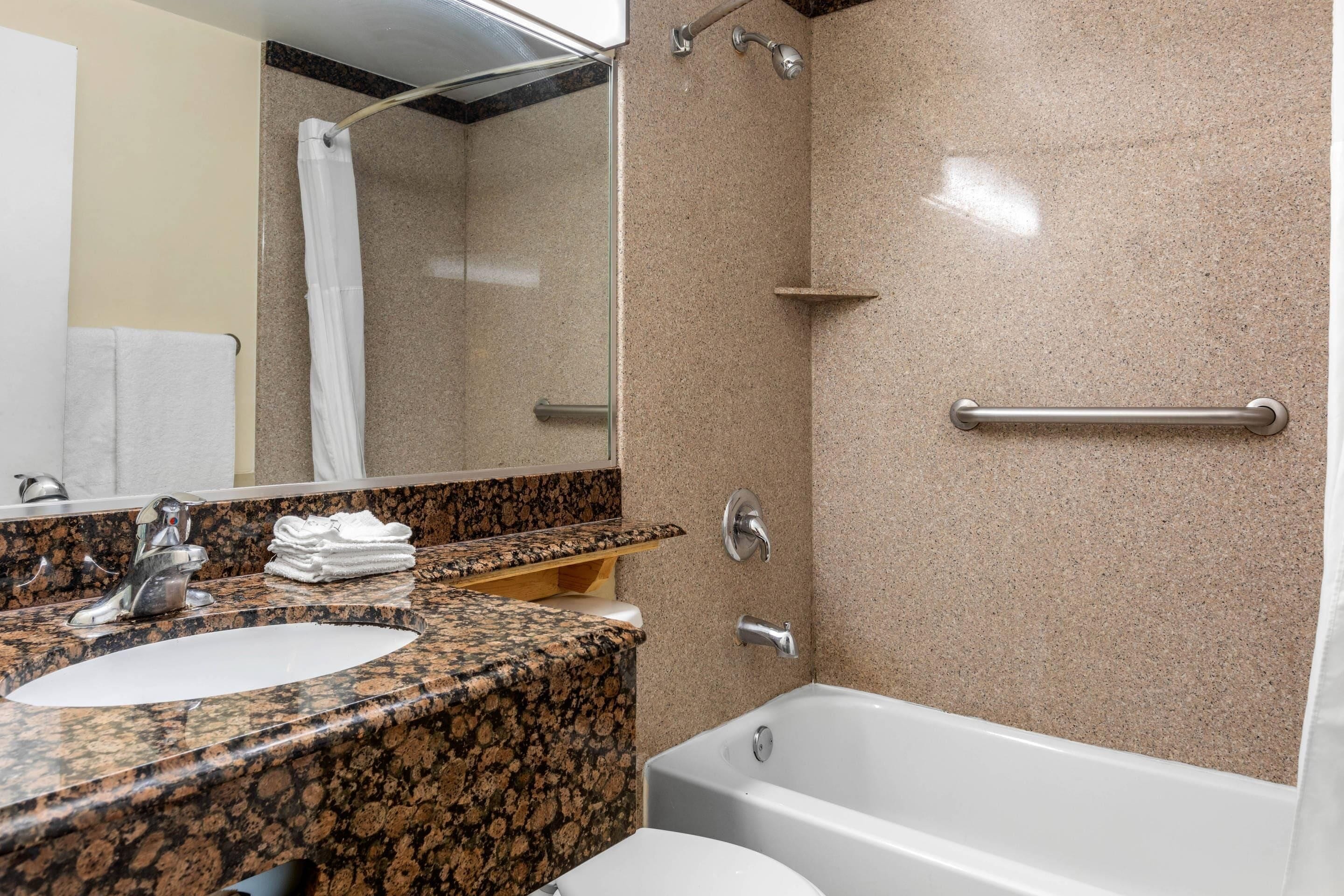 Une salle de bain avec un lavabo surmonté d’un plan de travail en granit, des toilettes blanches, une douche avec une porte en verre et un porte-serviettes.