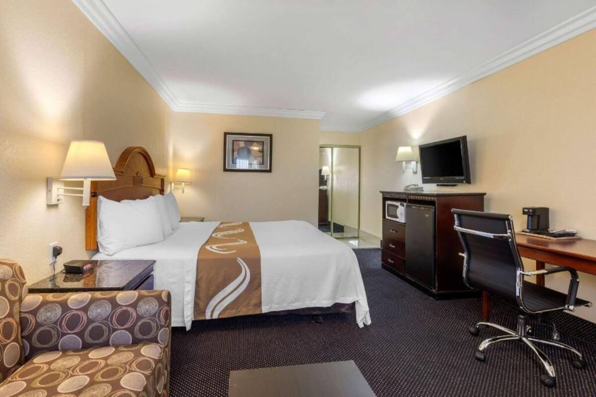 Una habitación de hotel con cama, escritorio, silla, televisor y una pequeña kitchenette.