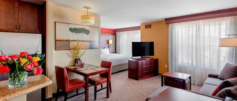 A hotel room with a dining area, a bed, a TV, and a window with curtains.