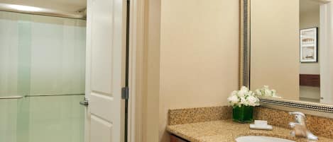 A bathroom with a granite countertop, a white sink, a mirror, and a glass shower enclosure.