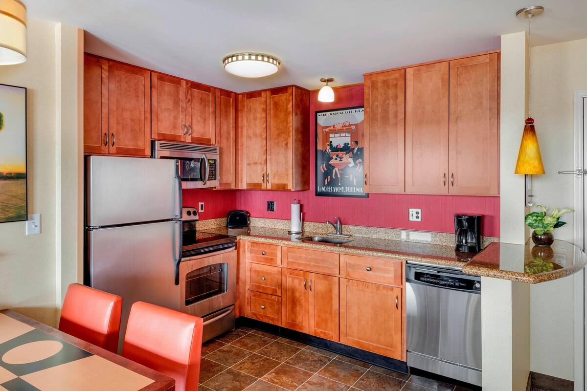 Una cocina compacta con armarios de madera, electrodomésticos de acero inoxidable y una zona de comedor con sillas rojas.