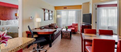 Una habitación de hotel con cama, escritorio, sofá, mesa de comedor con sillas y televisión.