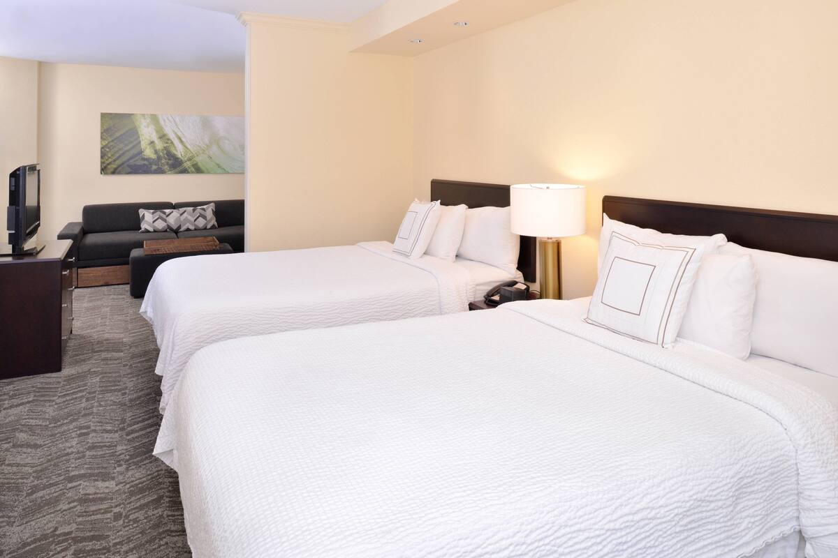 A hotel room with two beds, a sofa, a TV, and a painting on the wall.