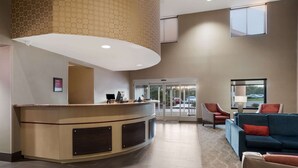 A reception area with a curved counter, a seating area with a blue sofa and red chairs, and a glass door entrance. - Comfort Suites Suffolk - Chesapeake (Suffolk)