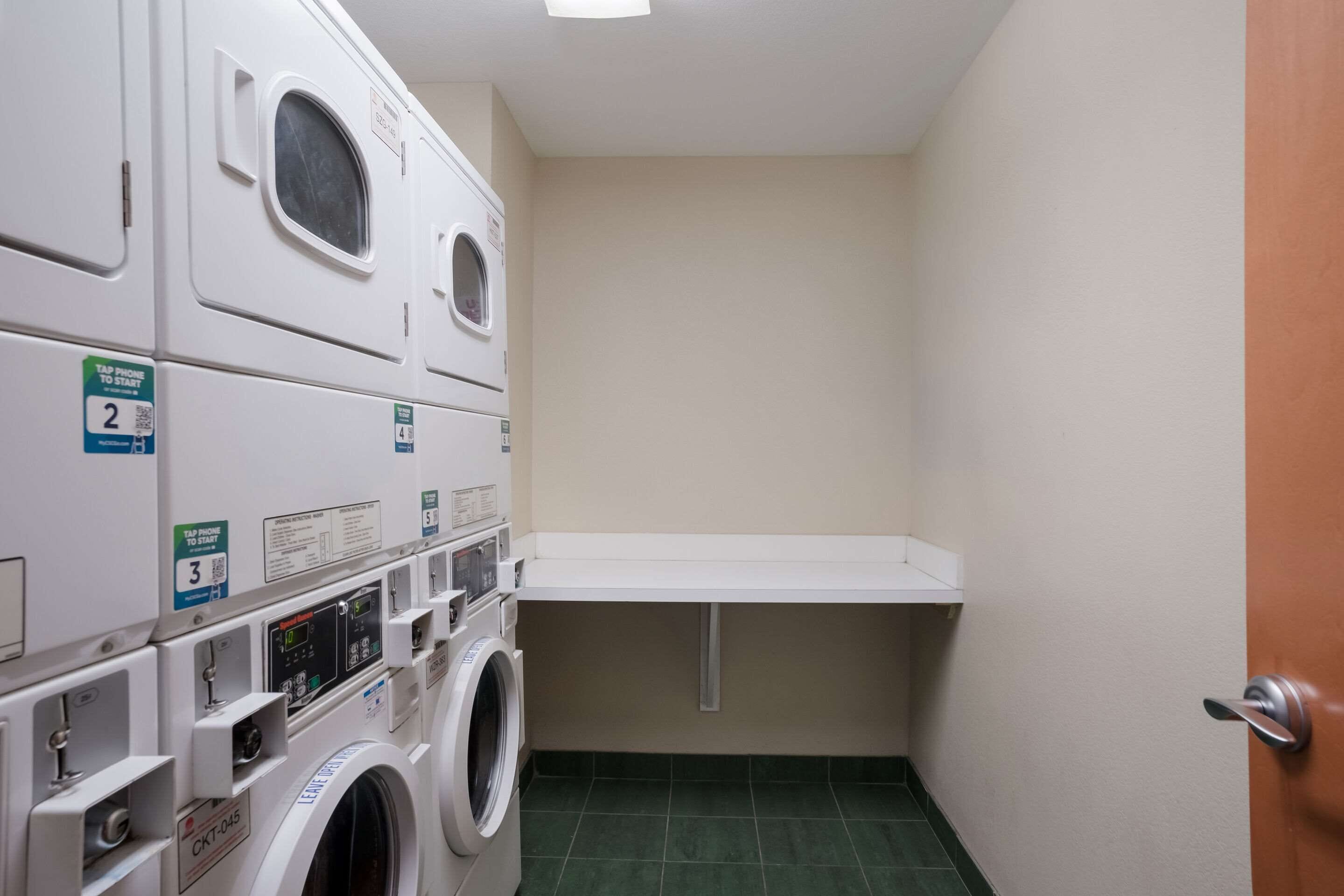 A laundry room with stacked washers and dryers, numbered signs, and a door.