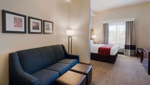 A hotel room with a blue sofa, a bed with a red blanket, a desk, and a lamp. There are three framed pictures on the wall. - Comfort Suites Suffolk - Chesapeake (Suffolk)