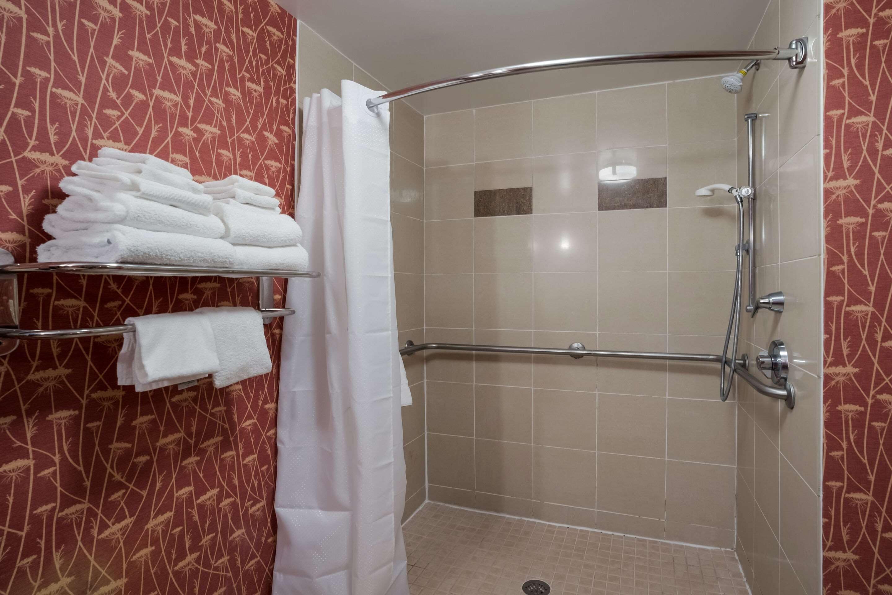 Zona de ducha con mampara de vidrio, toallero con toallas dobladas y panel de control de la ducha.