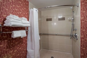 Zona de ducha con mampara de vidrio, toallero con toallas dobladas y panel de control de la ducha.