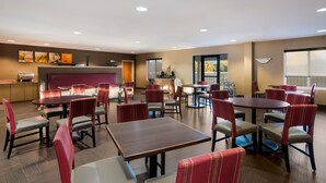 A hotel dining area with multiple tables and chairs, a kitchen area, and large windows offering views. - Comfort Suites Suffolk - Chesapeake (Suffolk)