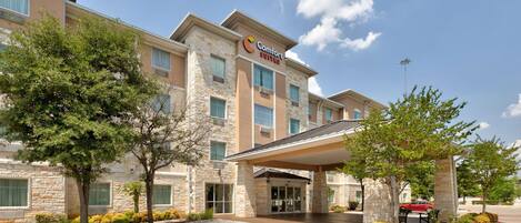 Ein Comfort Suites Hotel mit Steinfassade, großen Fenstern und einer überdachten Eingangshalle.