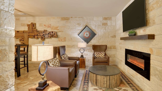 Una sala de estar acogedora con paredes de piedra, chimenea, sofás de cuero, una mesita de centro y un televisor de pantalla plana sobre la chimenea.
