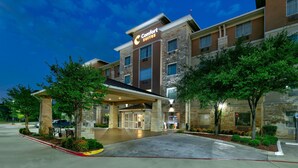 Un hotel Comfort Suites con fachada de piedra, entrada cubierta y jardines ajardinados.