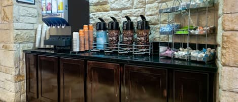Eine Kaffeestation mit Wasserspender, Kaffeetassen und einer Tassenhalterung an einer Steinwand.