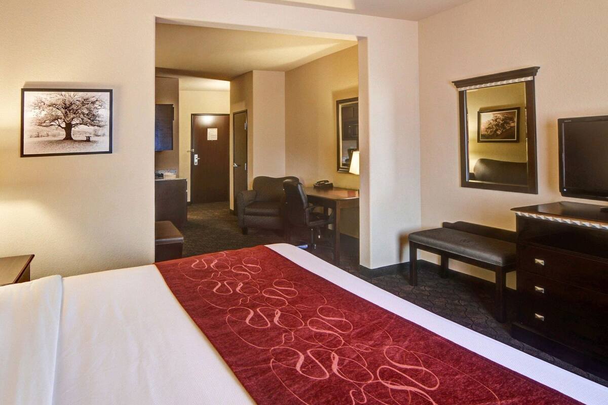 A hotel room with a bed, a desk, a chair, a television, and a door leading to another room.