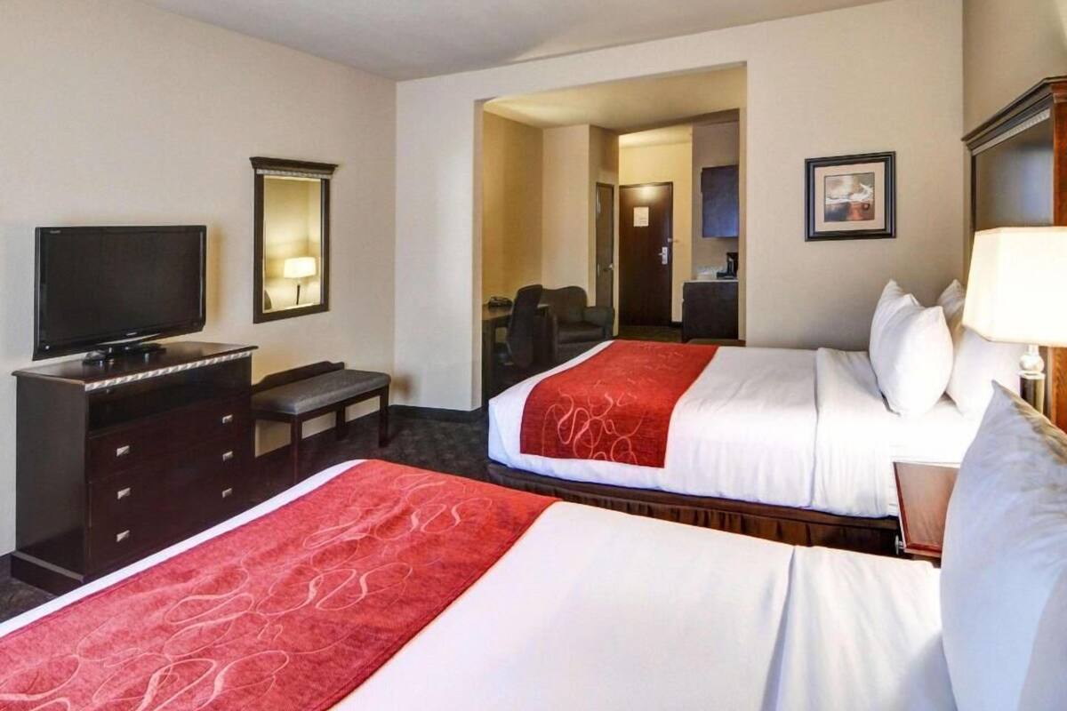 A hotel room with two beds, a TV, a desk, and a mirror.