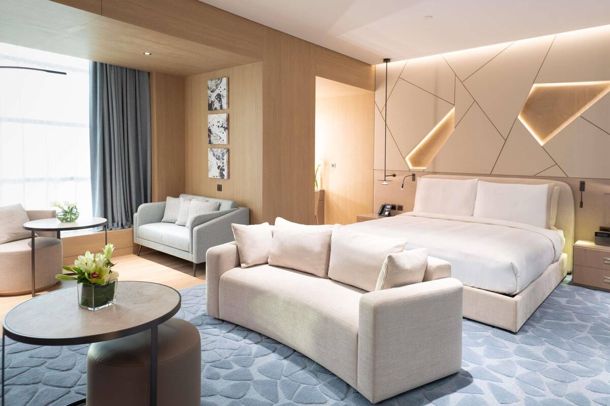 Quarto de hotel moderno com uma cama grande, um sofá, uma mesa pequena e obras de arte nas paredes.