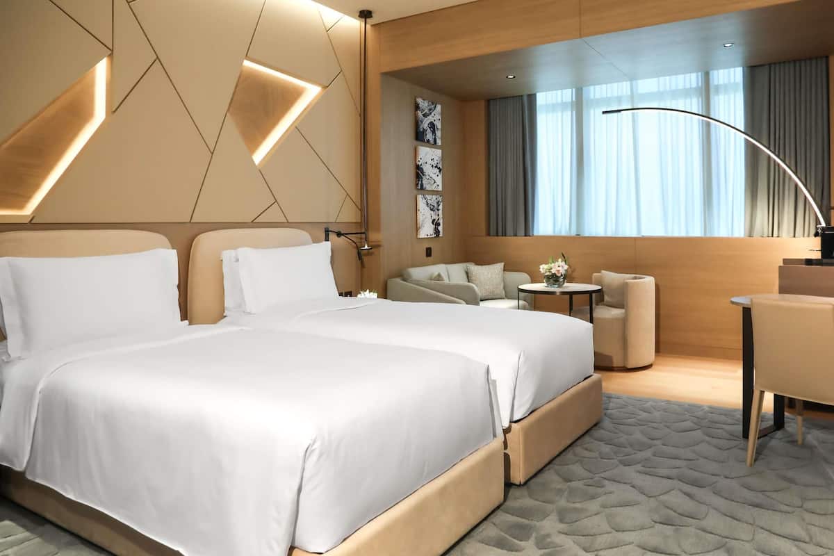 A modern hotel room with a large bed, a sofa, a small table with flowers, and a desk.