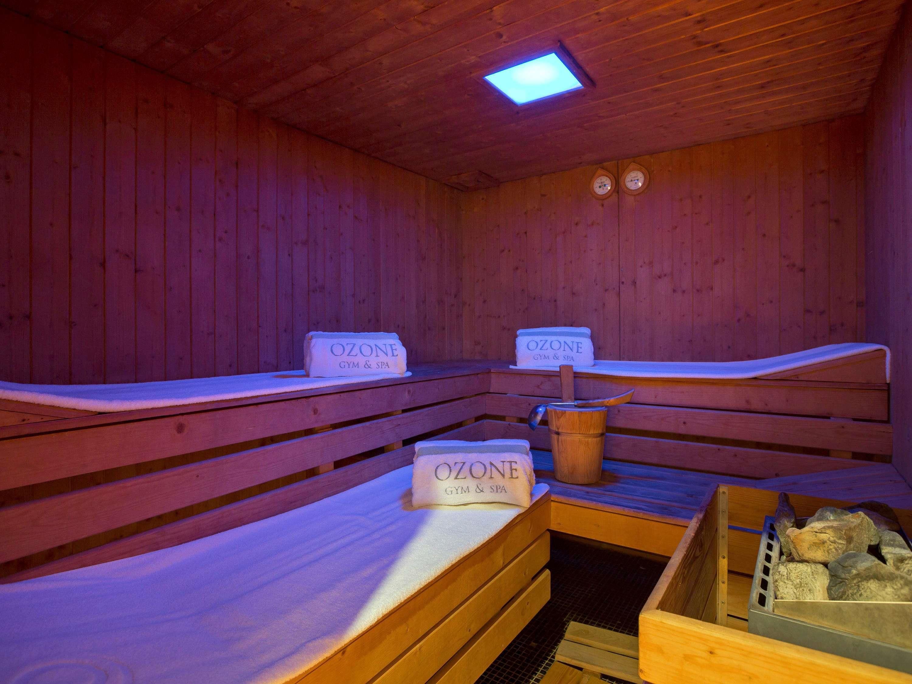 Una sauna con bancos de madera, un cubo y un recipiente con la etiqueta 'OZONE GYM & SPA'.