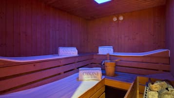 Una sauna con bancos de madera, un cubo y un recipiente con la etiqueta 'OZONE GYM & SPA'.