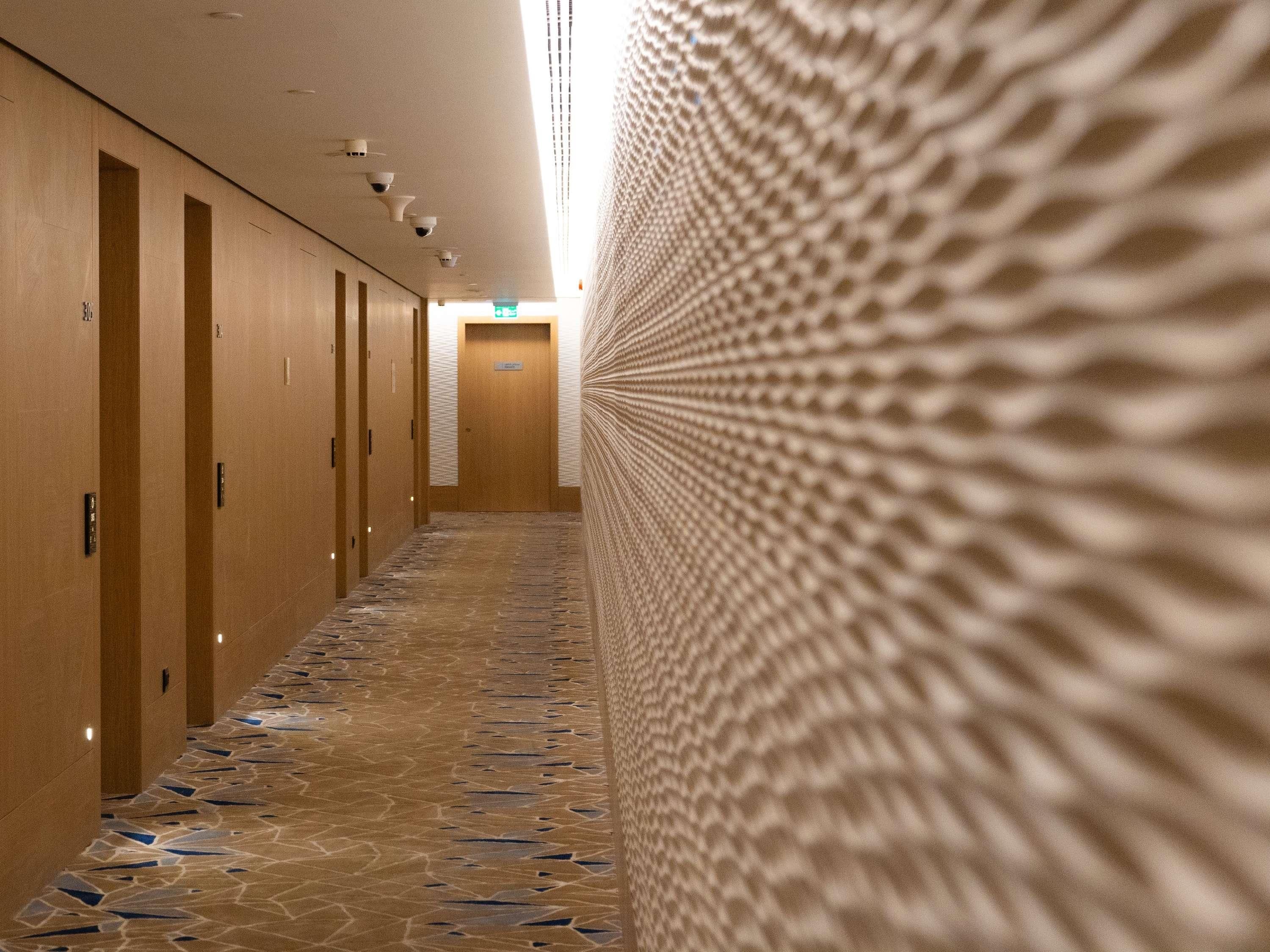 Un pasillo de hotel con un papel tapiz decorativo, puertas de madera y piso de baldosas.