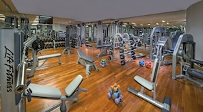 A gym with various exercise equipment, wooden flooring, and a mirrored wall. - La Cigale Hotel Managed by Accor (Doha)