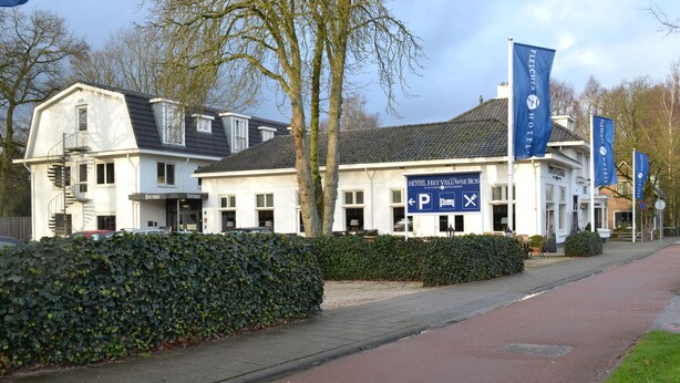 Un hôtel à la façade blanche, doté de nombreuses fenêtres et d’une enseigne indiquant un espace de stationnement.