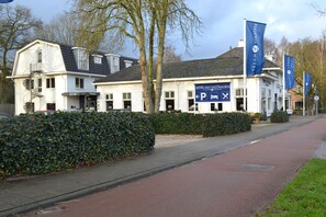 Un hôtel à la façade blanche, doté de nombreuses fenêtres et d’une enseigne indiquant un espace de stationnement.