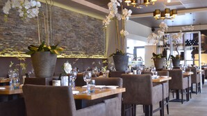 Un restaurant avec de nombreuses tables, des chaises et des orchidées suspendues.