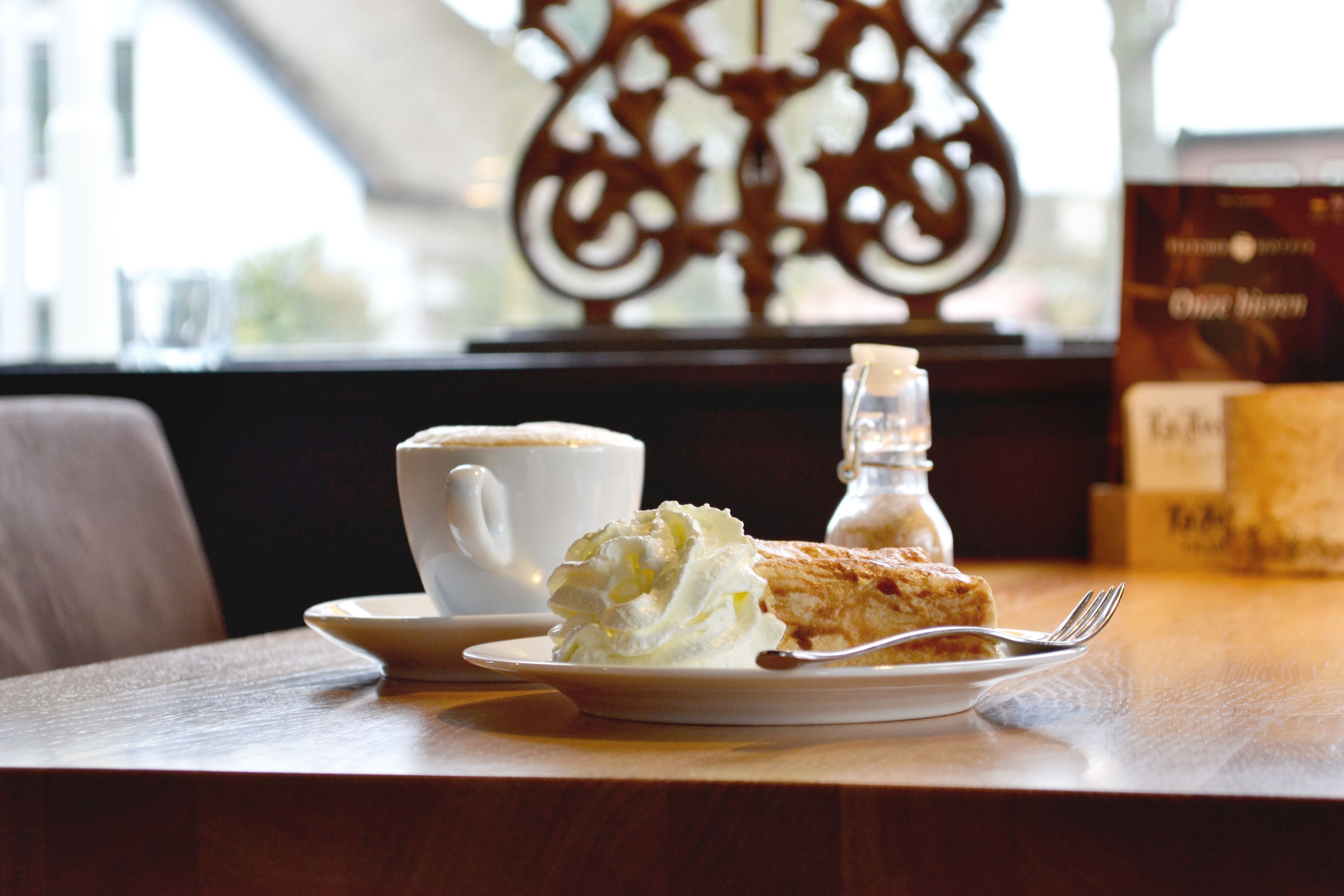 A dessert plate with a pastry and whipped cream, a cup of coffee, and a salt shaker on a table.
