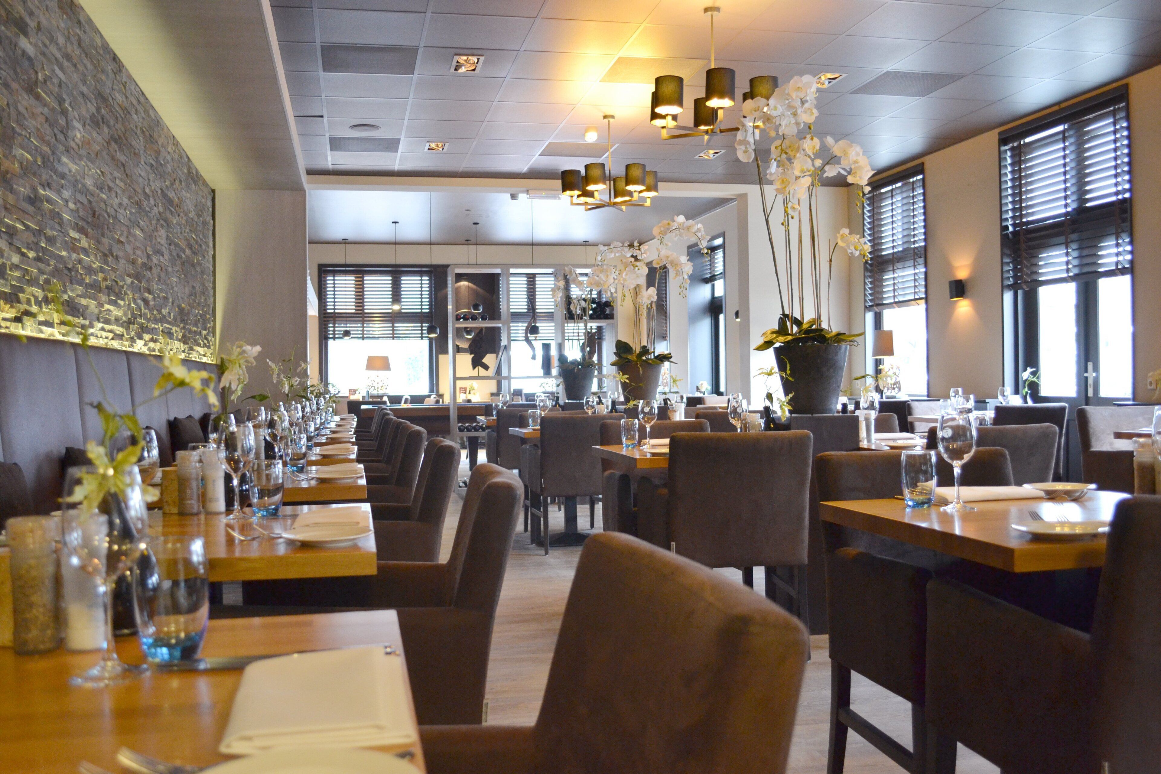 Een restaurantinterieur met lange tafels, stoelen en hangende lampen.
