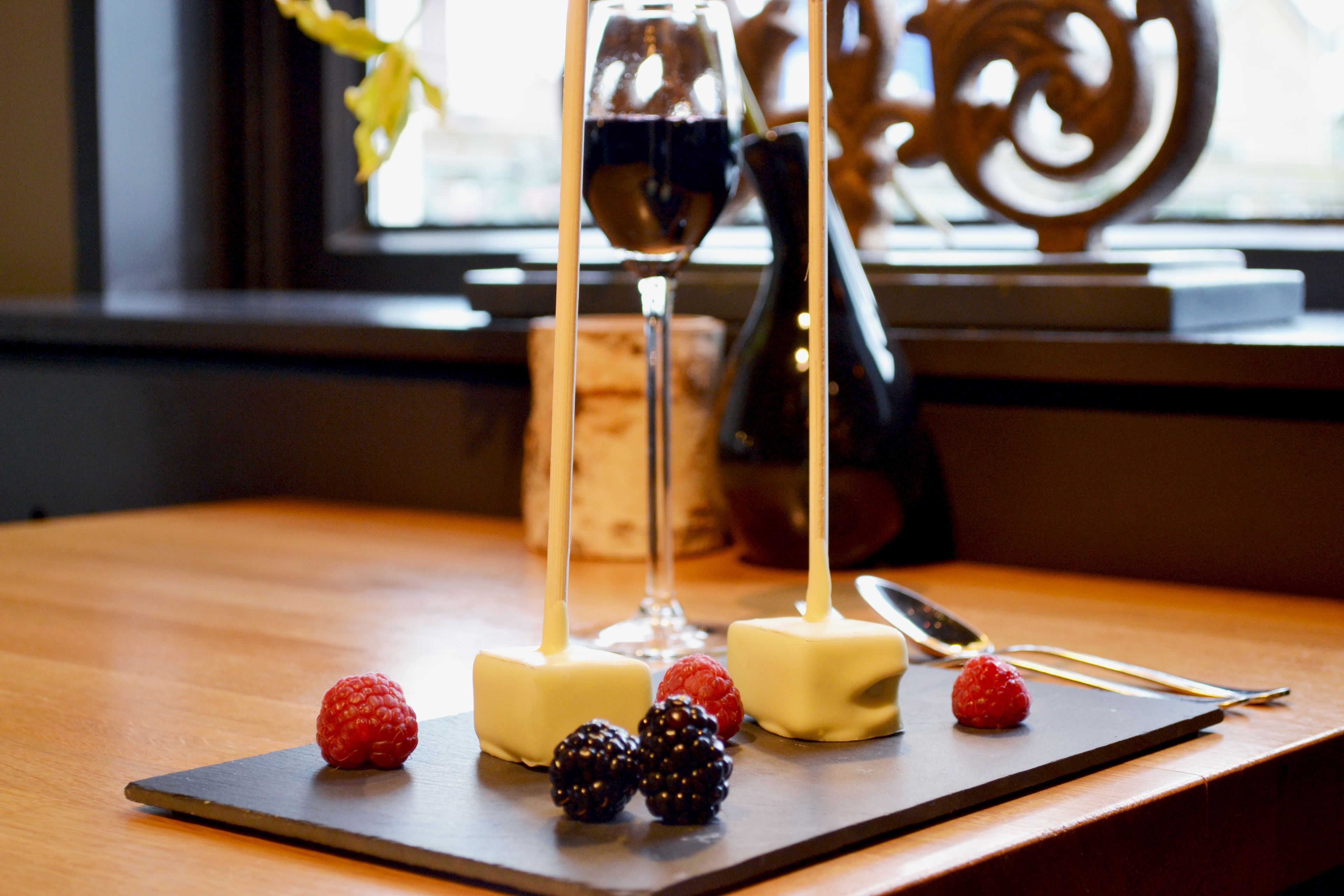 A wooden table with a chocolate-covered dessert, a glass of red wine, and a knife.