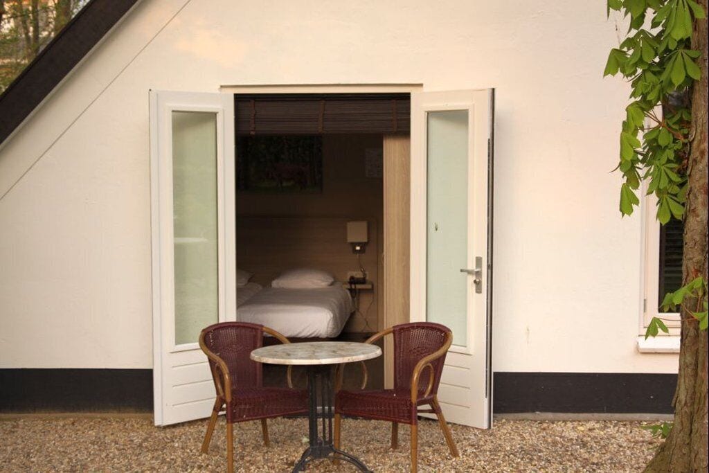 A small, private room with a bed, a round table, and two wicker chairs.