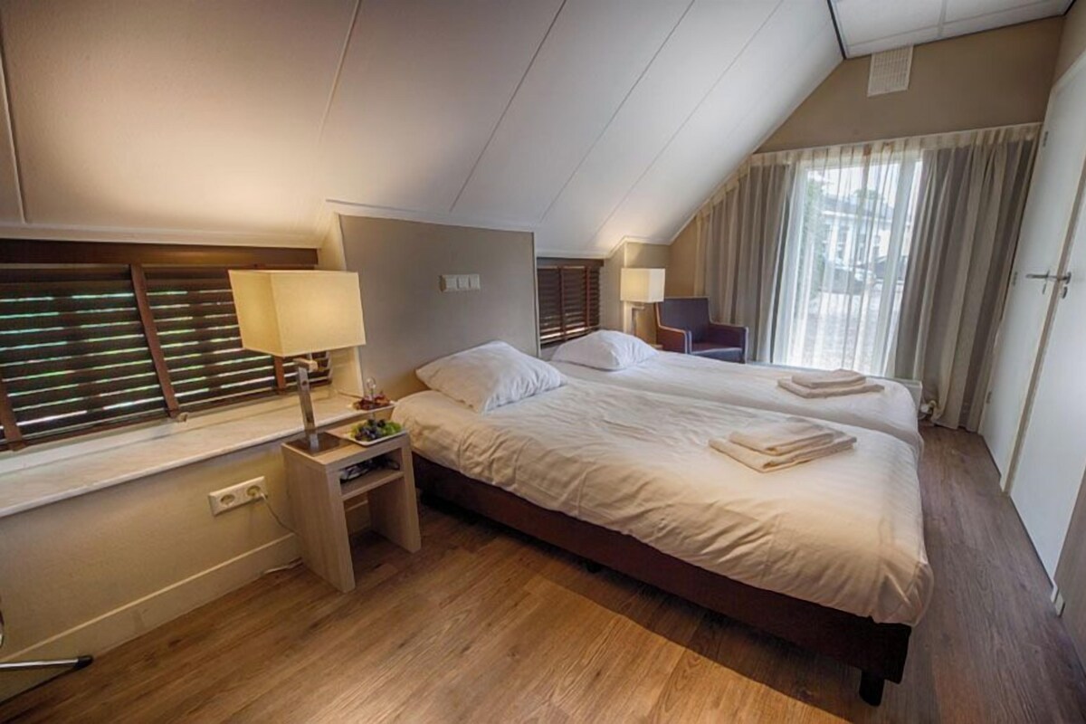 Ein Hotelzimmer mit Doppelbett, Nachttischen, einer Lampe, einem Sessel und einem Kleiderschrank.