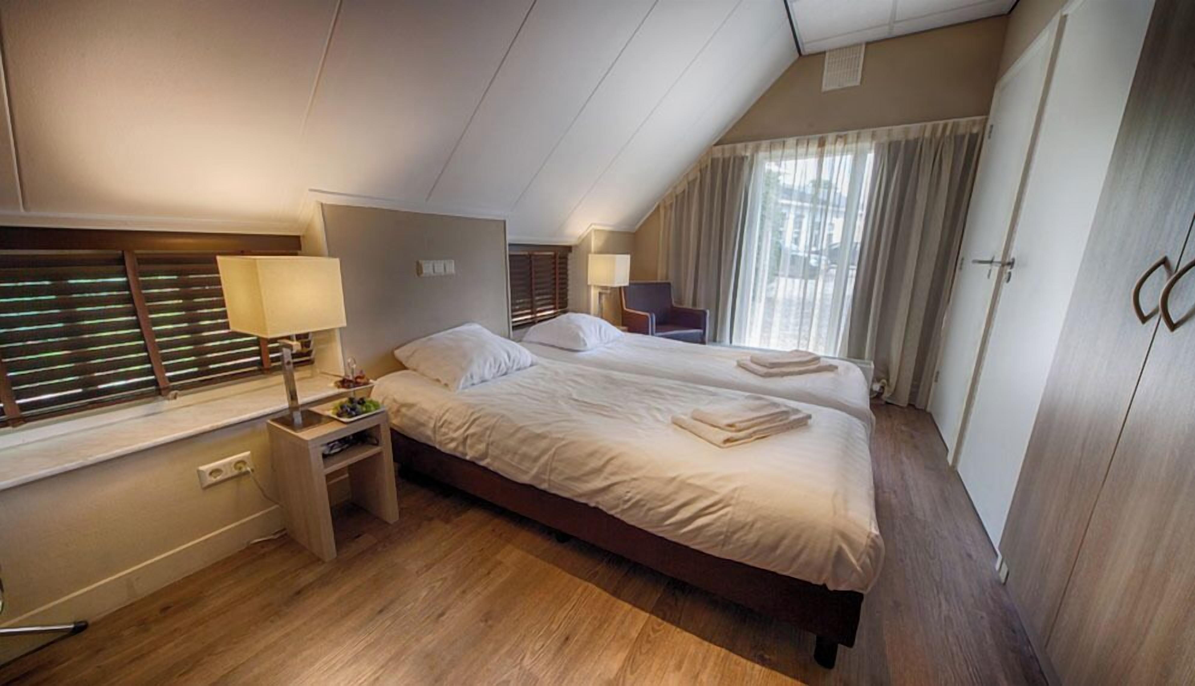 A hotel room with a double bed, bedside tables, a lamp, a chair, and a wardrobe.