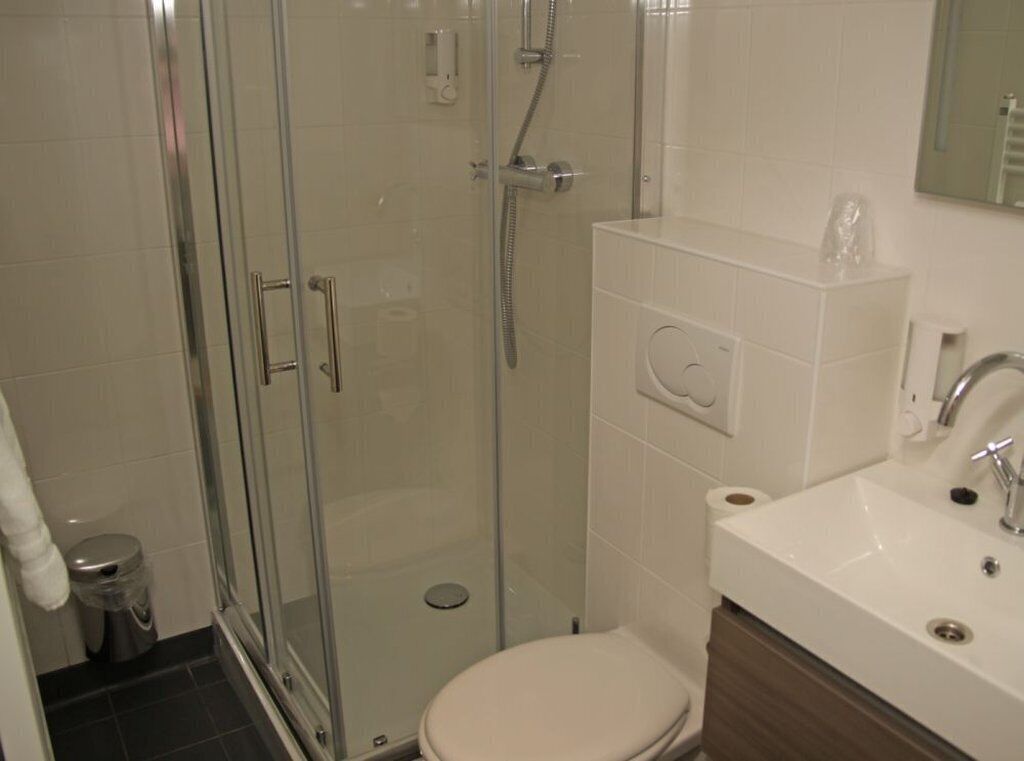Ein Badezimmer mit Duschkabine, Toilette und Waschbecken mit Spiegel darüber.