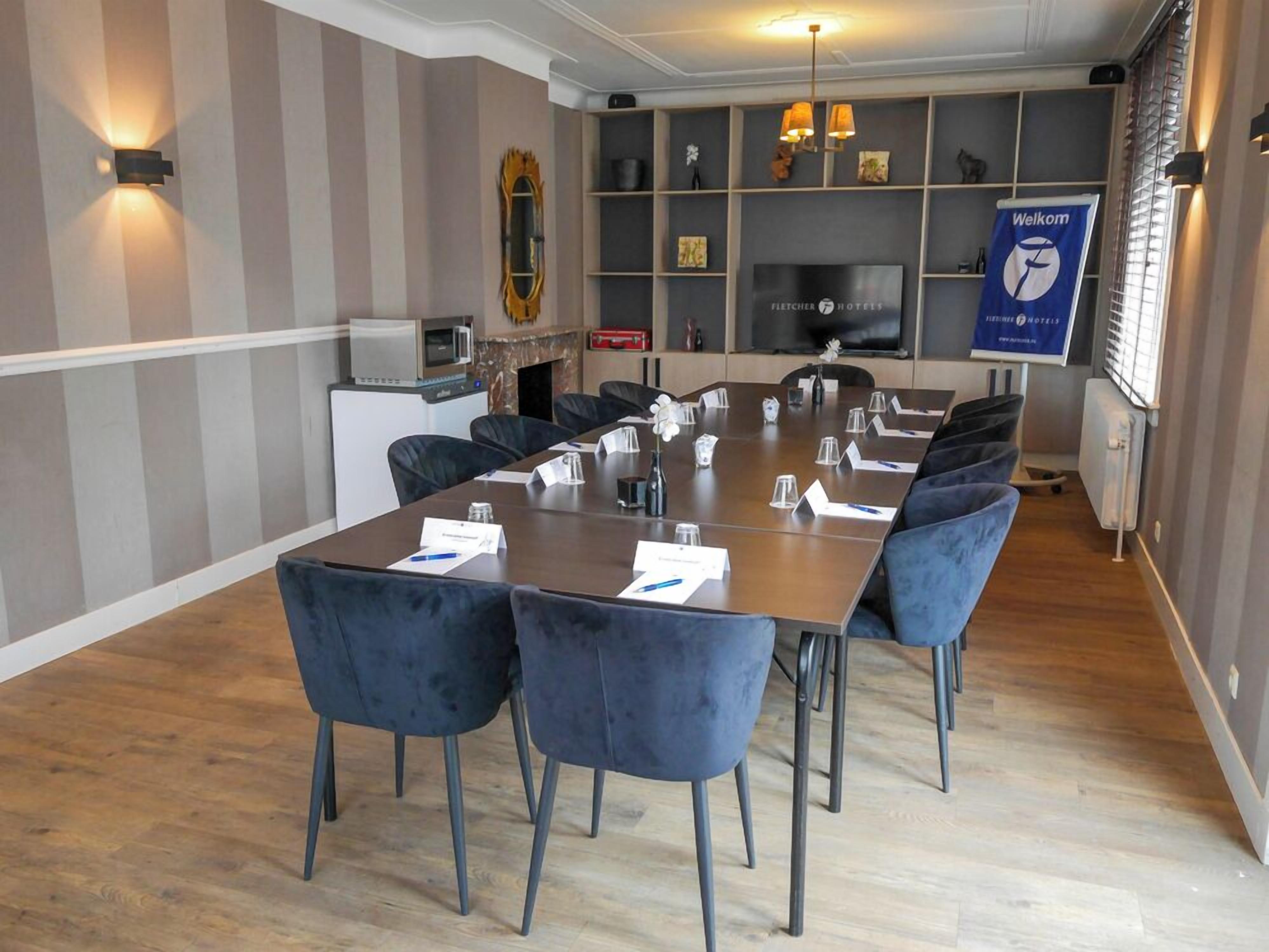 A conference room with a long table, chairs, name cards, and a 'Welkom' sign.