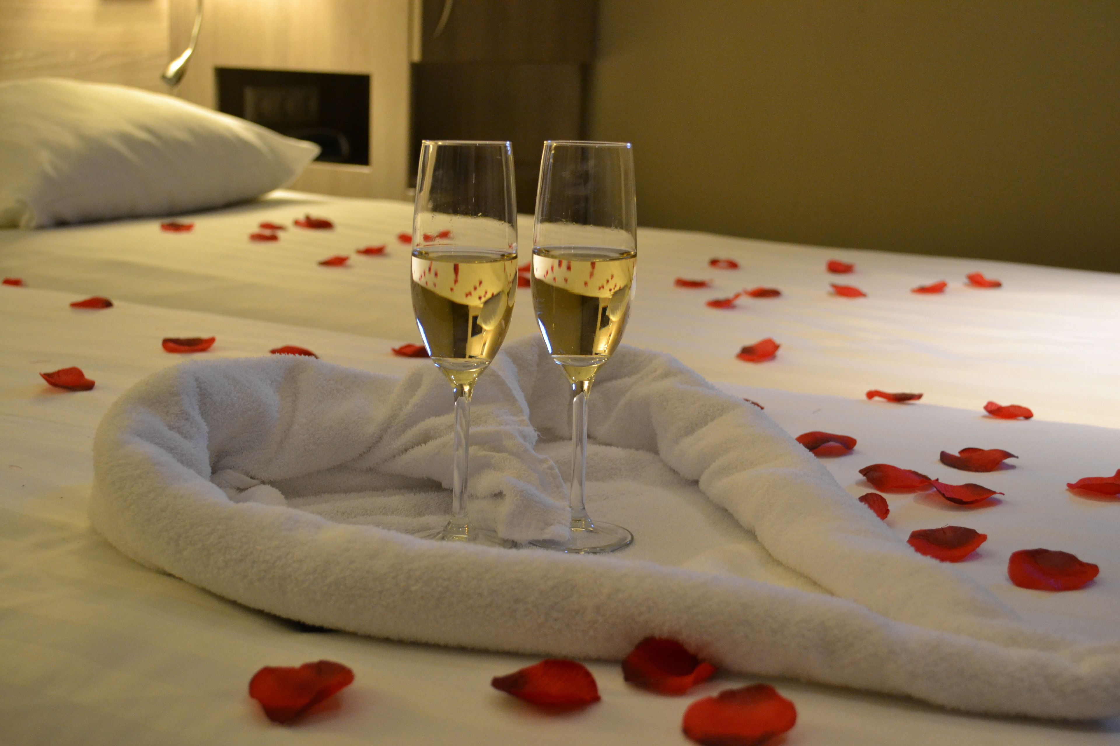 Een bed met rozenblaadjes en twee glazen witte wijn.