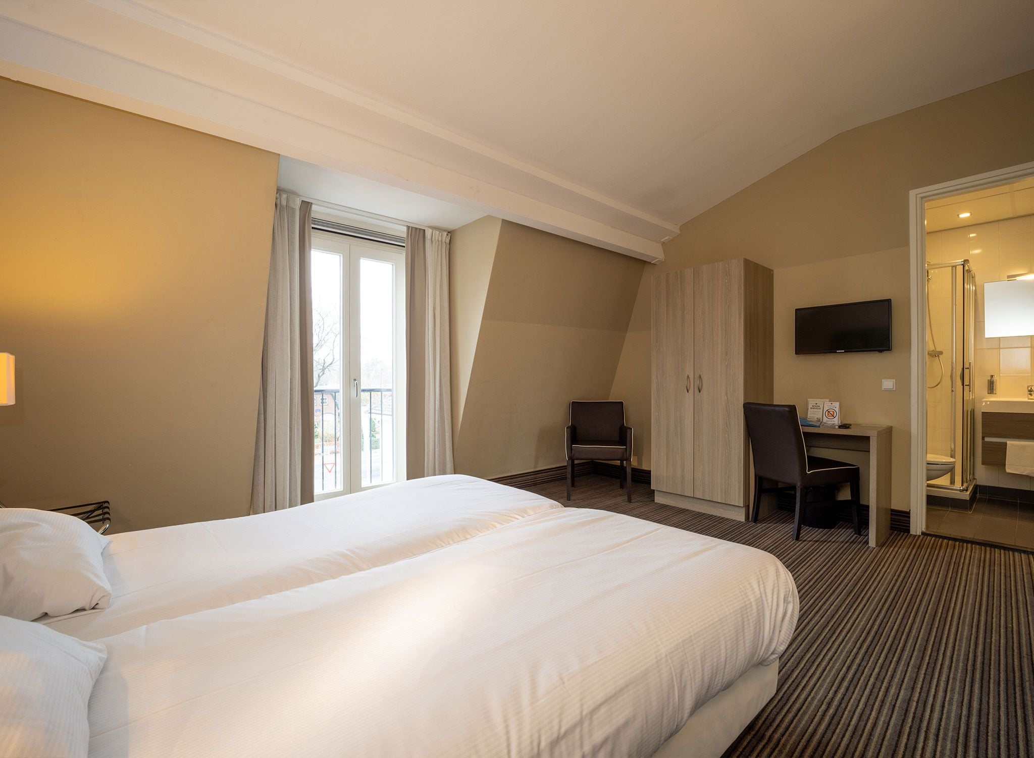 A hotel room with a large bed, a desk, a chair, a television, and a bathroom.
