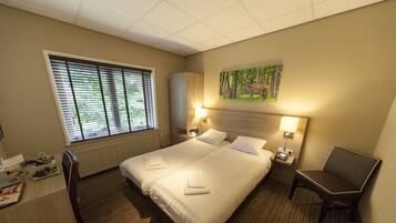Ein Hotelzimmer mit einem großen Bett, zwei Nachttischen, einem Schreibtisch mit Stuhl, einem Heizkörper und einem Fenster mit Jalousien.