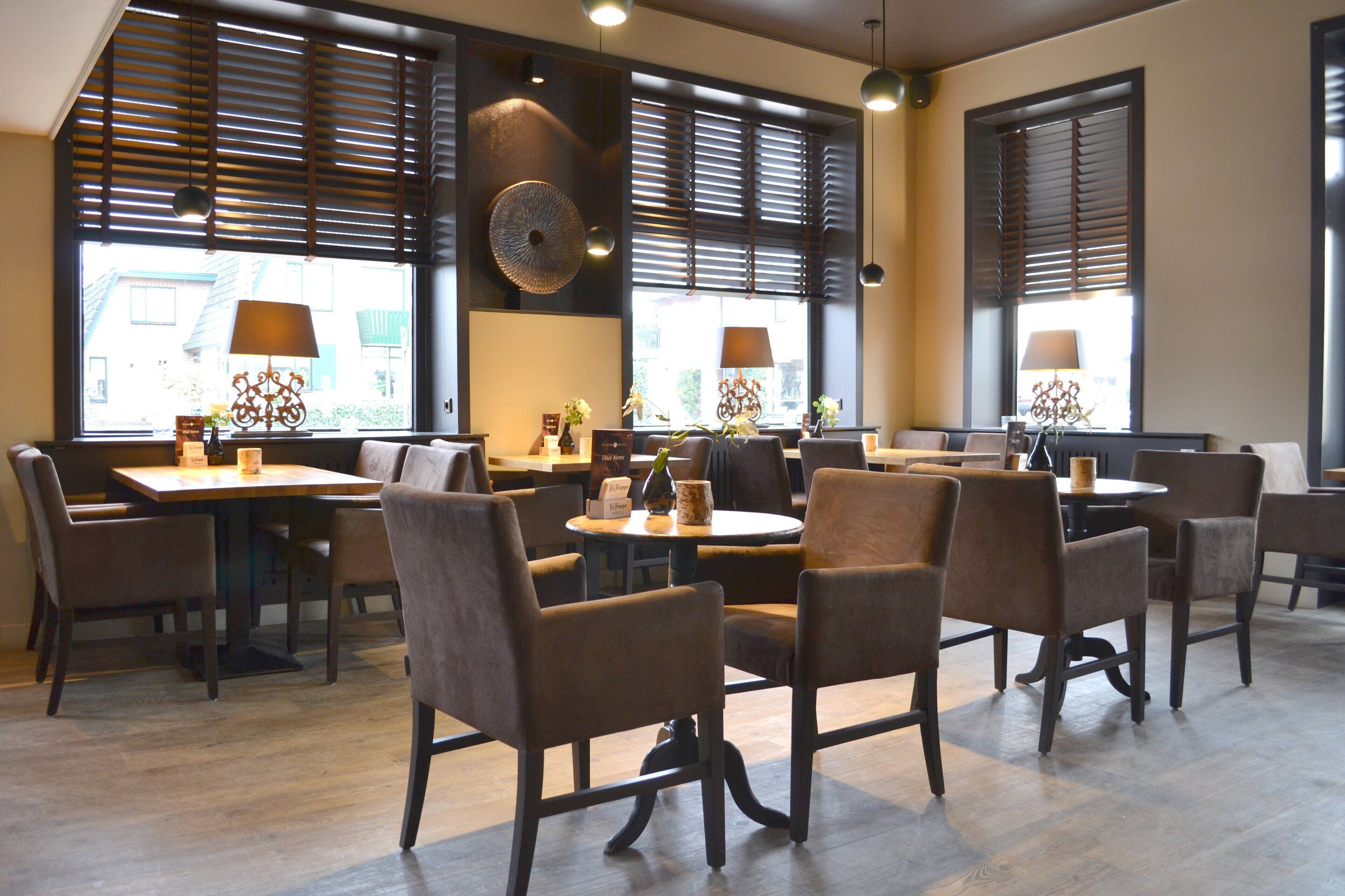 A modern dining area with multiple tables and chairs, large windows with blinds, and decorative wall art.