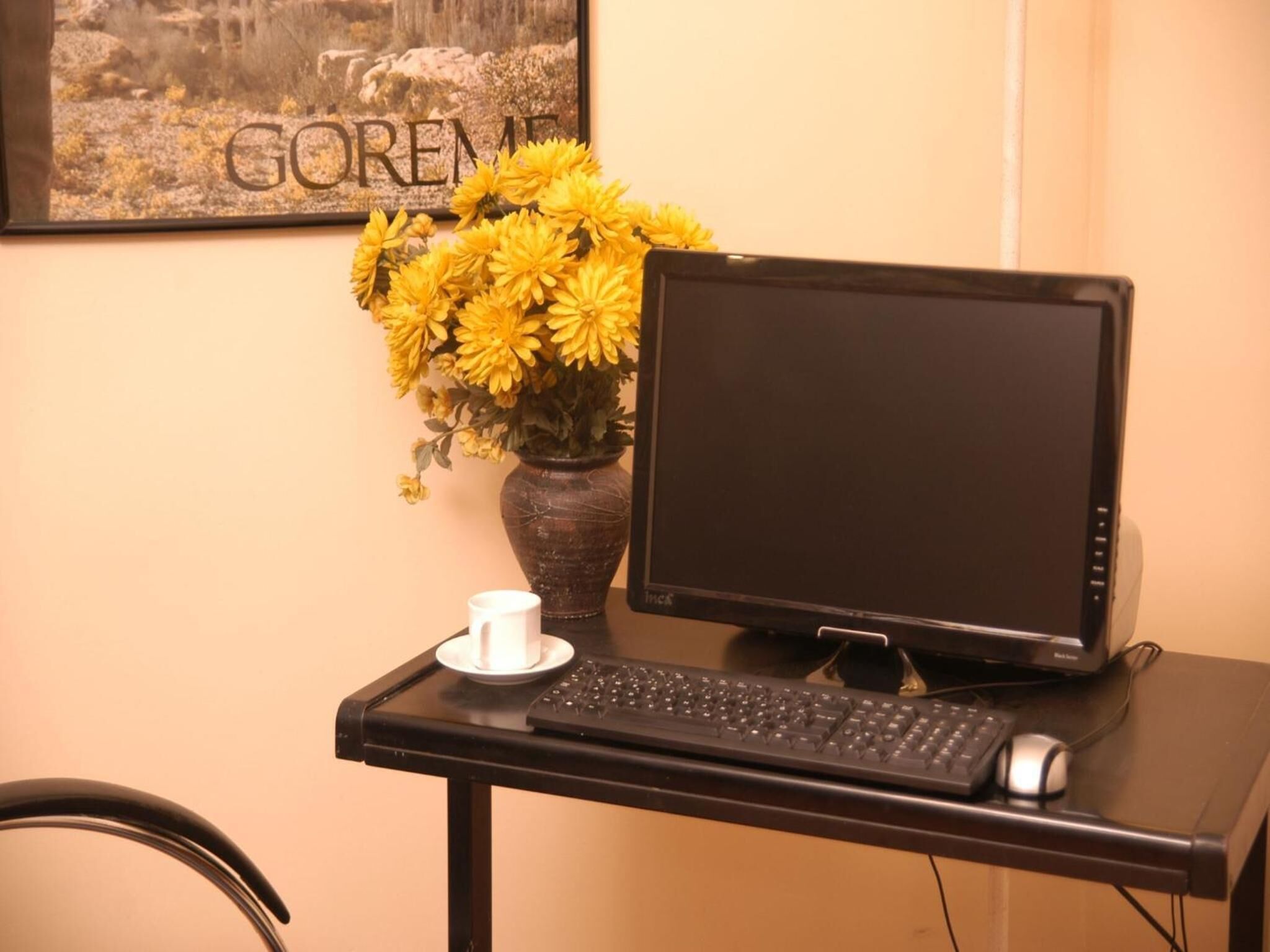 A desk with a computer monitor, keyboard, and a vase with yellow flowers.