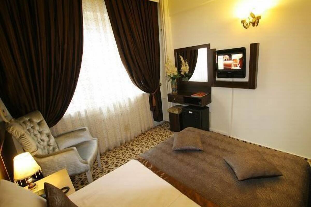 A hotel room with a bed, a chair, a desk with a TV, and a window with curtains.