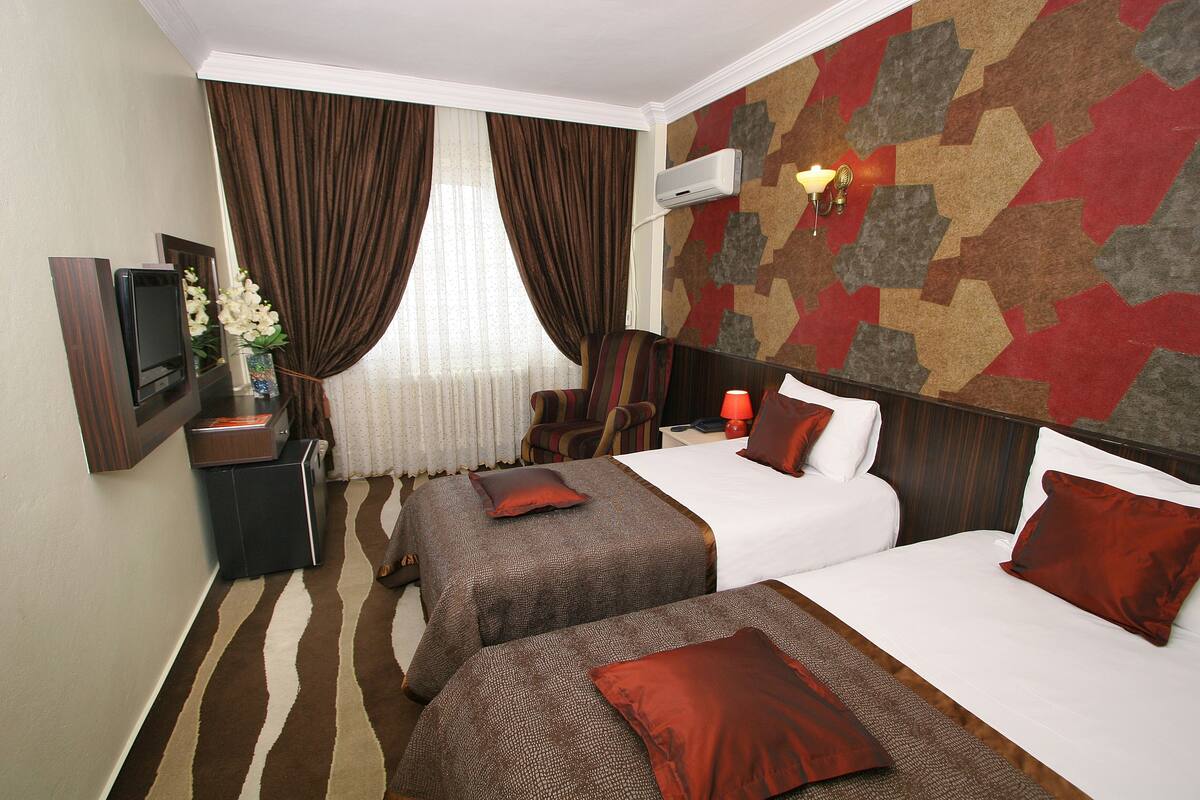A hotel room with two beds, a TV, a desk, a chair, and a patterned wall.