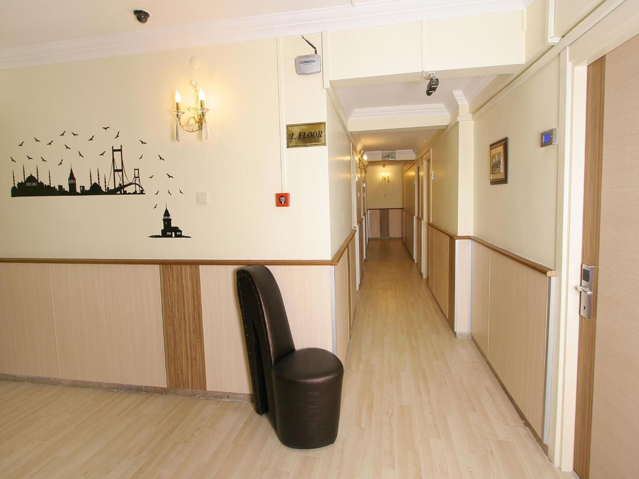 A hotel corridor with a wooden floor, a wall-mounted trash bin, a coat rack, and a sign indicating the floor level.